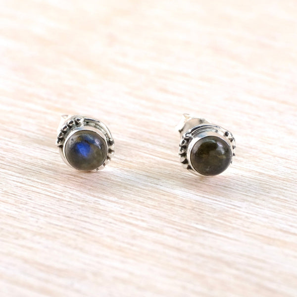 Pair of silver stud earrings with blue gemstones on a light wood background