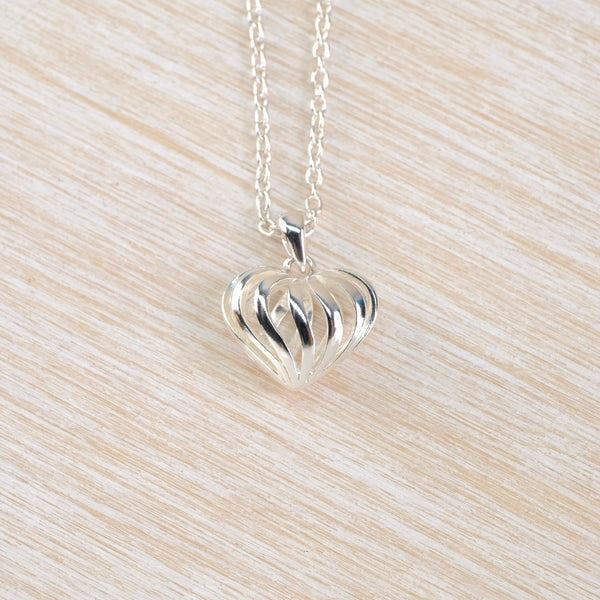 A silver heart shaped pendant on a chain. The pendant is ribbed and 3-dimensional