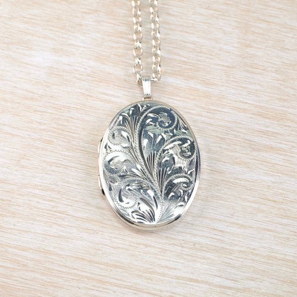 Silver floral-patterned locket on a chain against a beige background