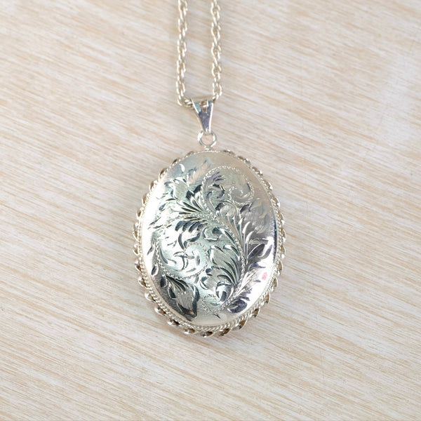 Silver engraved locket on a chain against a beige background