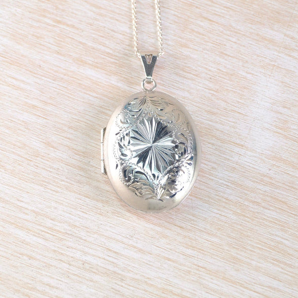 Silver locket with intricate design on a light wood surface