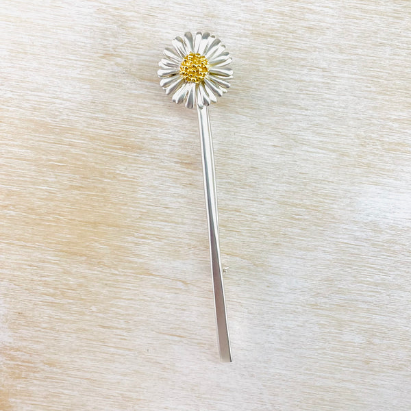 A ong slender brooch featuring a full-face daisy flower on a long stem.Finished in soft satin silver with heavily gold plated detal at the centre of the flower, andlovely delicate detila o the petals.