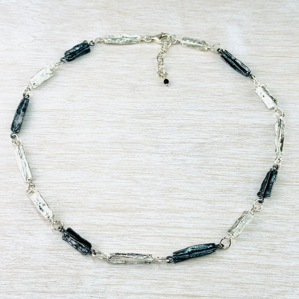 Textured and oxidized silver link necklace with a lobster clasp, displayed on a wooden surface.