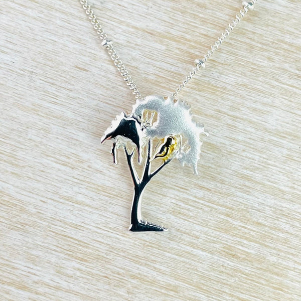 A sterling silver tree-shaped pendant with gold detailing and a bird sitting in the branches, presented on an 18 inch beaded curb chain. A sterling silver tree-shaped pendant with gold detailing and a bird sitting in the branches, presented on an 18 inch beaded curb chain.