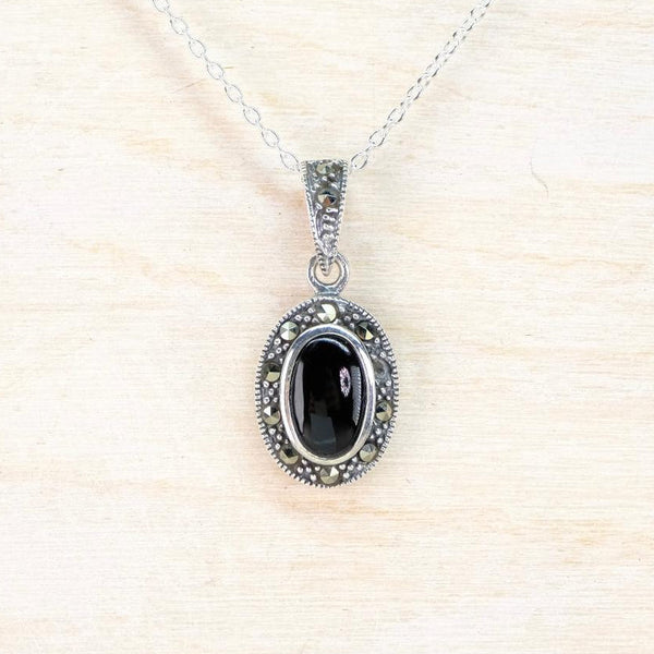 Silver pendant with oval black stone  surrounded by marcasite stones on a white background