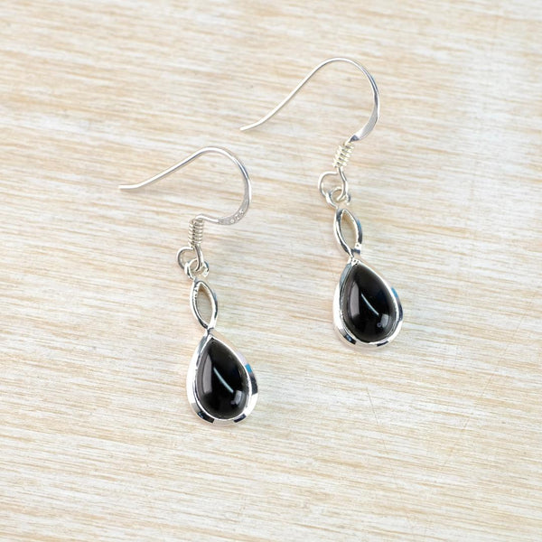 Black teardrop earrings on silver hooks on a light wood surface Black teardrop earrings on silver hooks on a light wood surface
