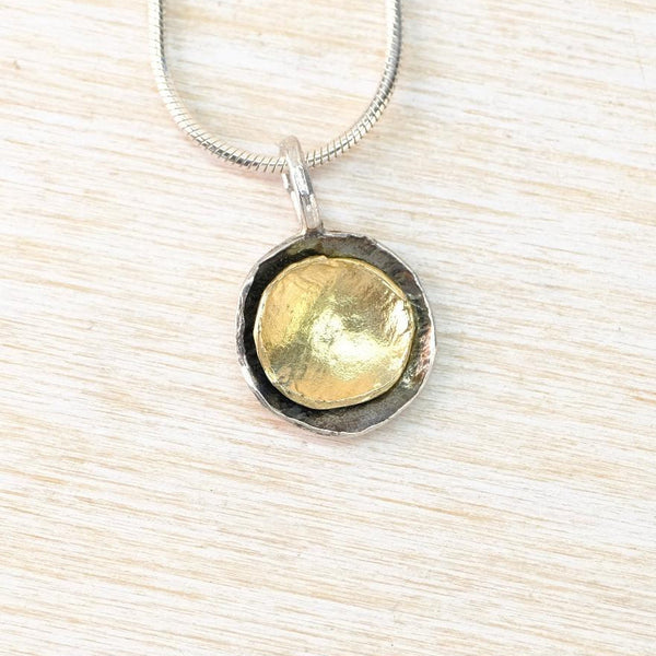 Necklace with a gold and silver pendant on a light wood surface