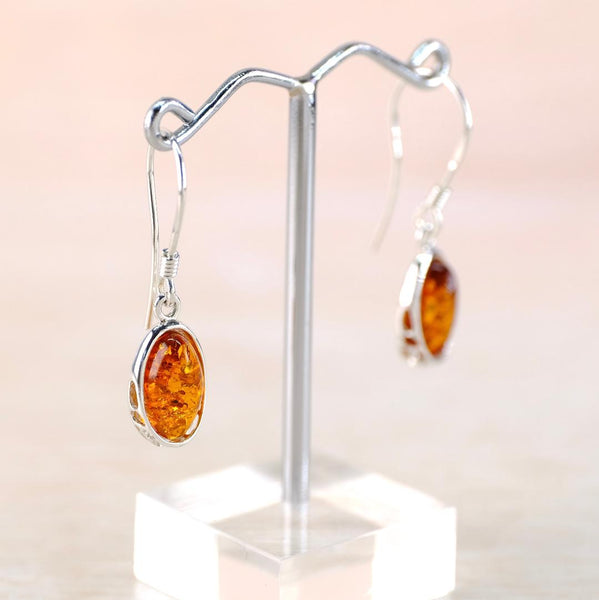 Silver earrings with amber stones on a stand against a light background