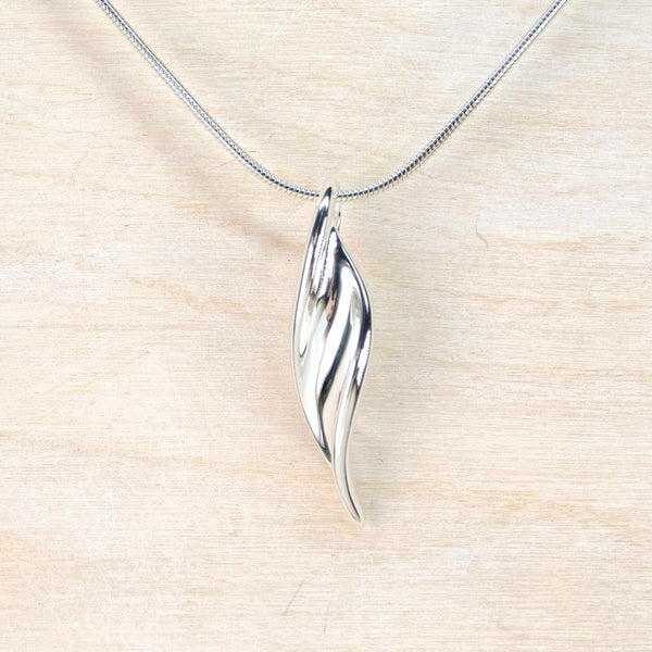 Silver leaf-shaped pendant on a chain against a beige background Silver leaf-shaped pendant on a chain against a beige background