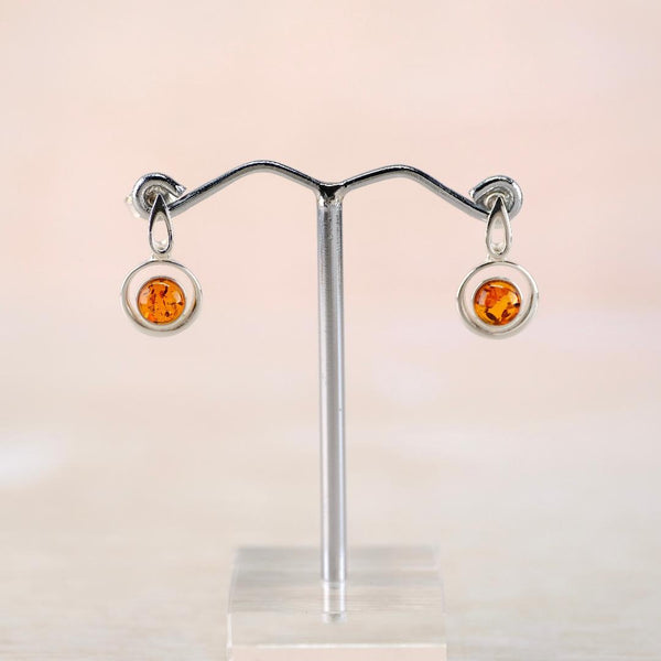 Silver earrings with amber stones on a stand against a light background