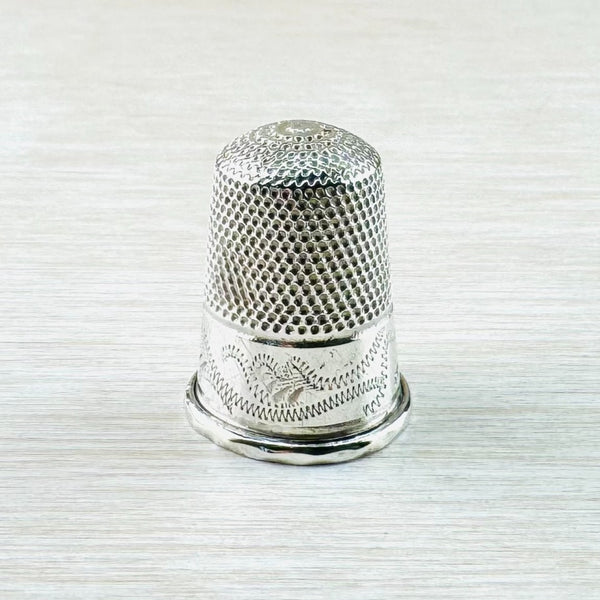  The top half of the thimble has repeated little dots, the bottom half has  a swirl design that looks a little like a zip. The bottom band is plain shiny silver with a visisble hallmark.