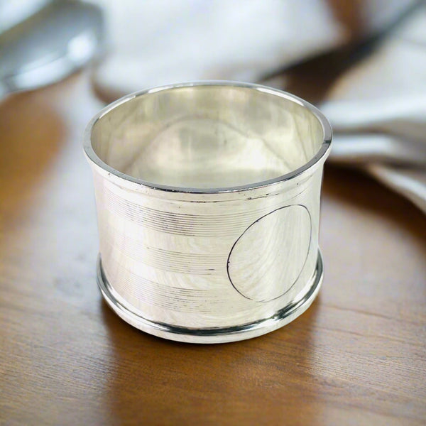 Round napkin ring with shiny rims top and bottom. The decoration is three sets of horizontal stripes., ten in each group . A round plain cartouche is  empty at the front.