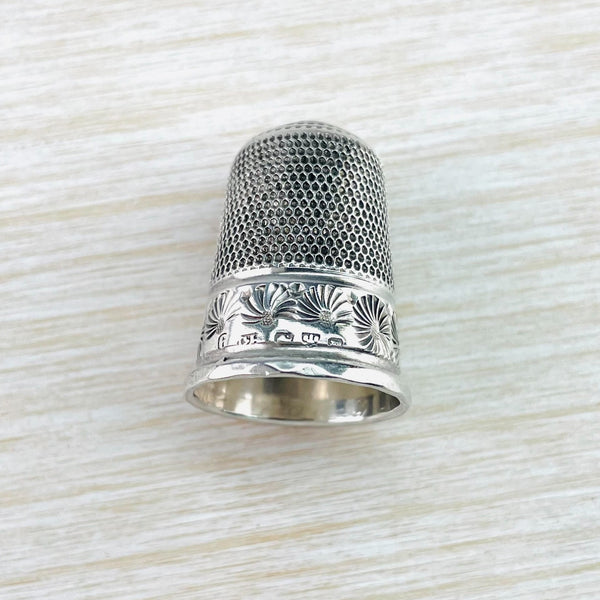 silver thimble with two different designs in two halves. The top is lots of little dots, the bottom is larger flower design, a little like a chrsanthemum. Their is a plain silver band around the bottom.