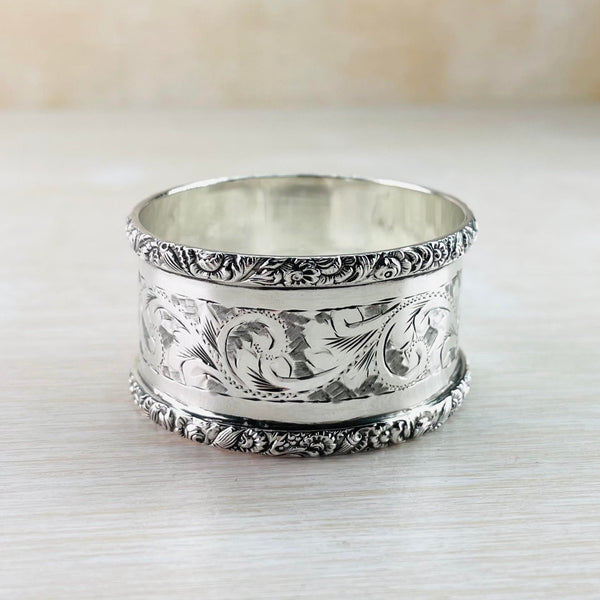The top and bottom rims have a very detailed design of flowers and leaves. There are then two plain polished silver stripes and a central swirly design.