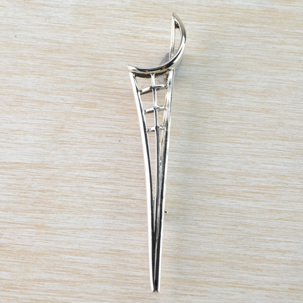 A slender long thin brooch. The top is an open semi circle set at an angle . From this a sword shape comes down to a point with a central stripe and three horizontal stripes forming a grid at the top,