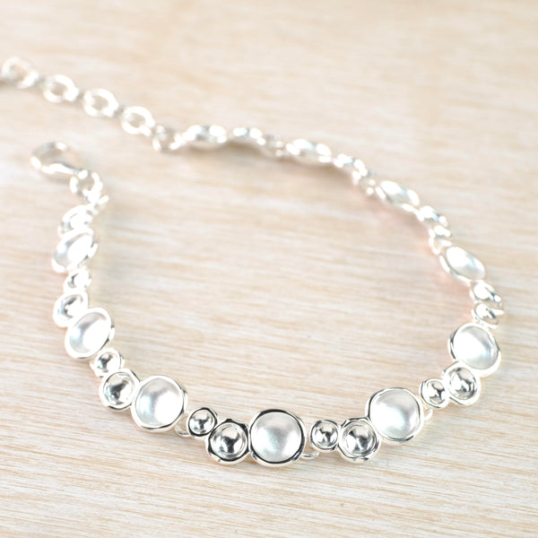 Bracelet formed of concave discs in different sizes and finishes. In groups of three - a larger satin finished one then a medium and a small high polished. Discs go all around the bracelet and it has a small piece of chain at the end.