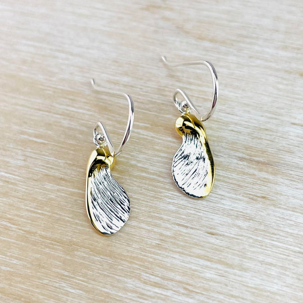 earrings shaped as sycamore wings with textured silver edged with gold colour. Hanging off a silver hook.
