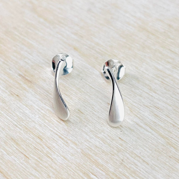 A pair of matt silver droplet stud earrings on a white background.