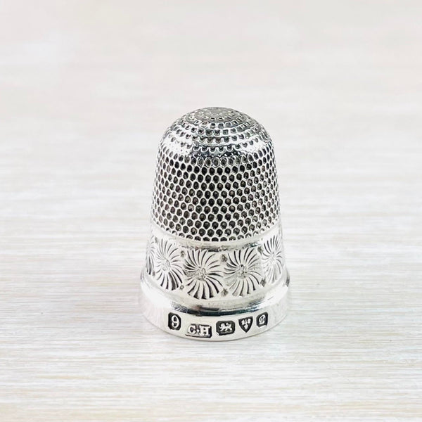 ilver thimble with two different designs in two halves. The top is lots of little dots, the bottom is larger flower design, a little like a chrsanthemum. Their is a plain silver band around the bottom. The hallmark is clear.