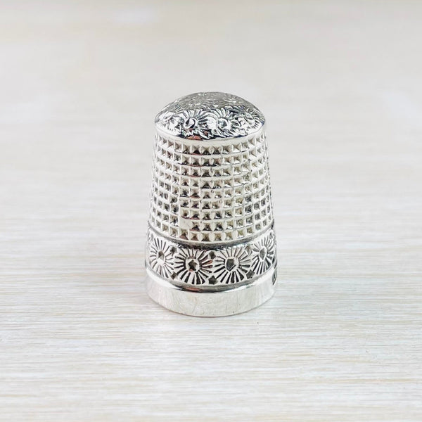 Silver thimble with a square geometric design hammered in to the top two thirds an a starburst effect design in a stripe underneath that. The very bottom is plain high polished silver. The top of the thimble also has a pretty flower design covering it.