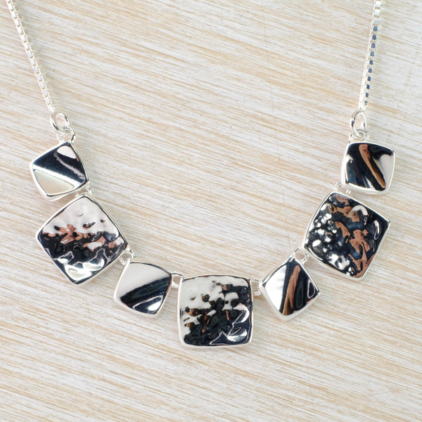 A half chain necklace - the front piece is formed of 7 square pieces that curve around, Four smaller high polished quares alternate with 3 larger hammered fini shed ones. This all hangs from a link chain.