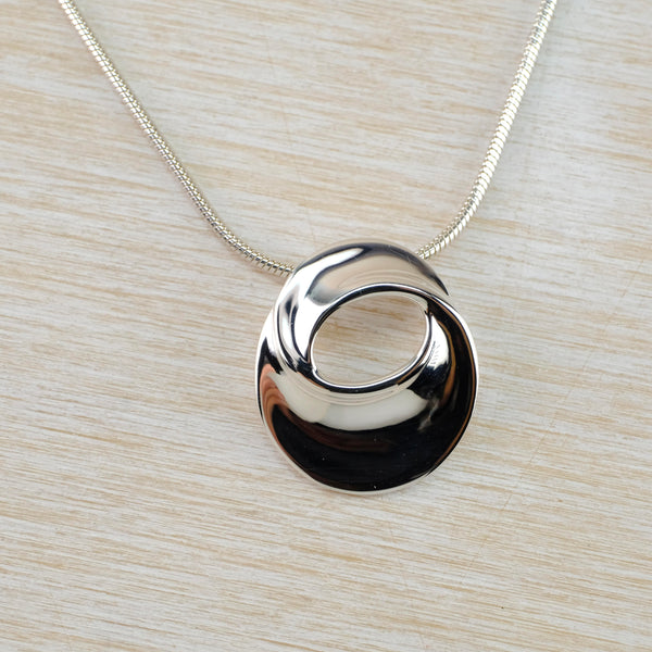 Very shiny oval shaped pendant with a gentle twist. There is an oval opening in the top half and a chain threaded behind .