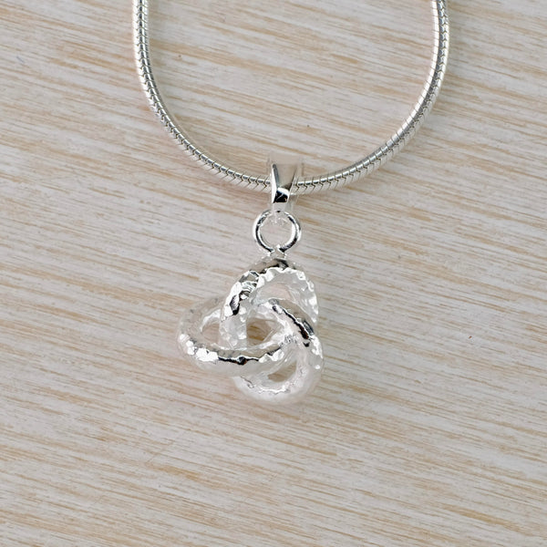 A small silver knot, with a hammered finish, hangs off a silver snake chain.