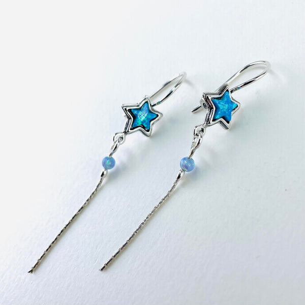 Long slender earrings set on a solid silver hook. At the top is a 5 pointed sparkly blue opal set into a star shaped surround. A silver ring from the bottom of the star is attached to a silver ring at the top of a silver chain. At the very top of the chain is a pretty pale blue, small round opal bead. The chain drop is slim and moves freely.