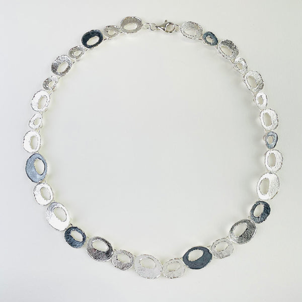 A necklace formed of off circle linkes with an off circle cut out.All are textured, some are dark oxidizes silver, some brighter. A necklace formed of off circle linkes with an off circle cut out.All are textured, some are dark oxidizes silver, some brighter.