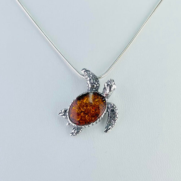 Cute turtle pendant. The body is formed of  a dark orange amber with lots of little inclusions, surrounded in a silver mount, slightly textured. Everything else is made from silver.One front flipper - well engraved to look like turtle skin appears to be holding on to the chain , the other sits at the side of the body. The two back flippers, again realistically marked are just on either side of the little tail at the back of the body. His head is tilted slightly to the side as if looking at the chain.