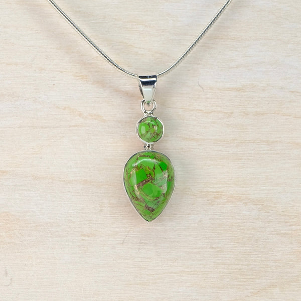 Green teardrop pendant on a silver chain against a beige background
