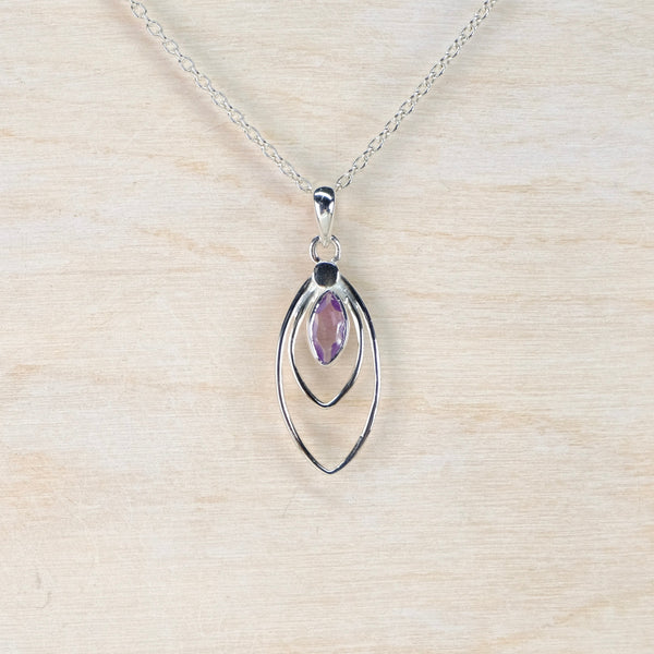 Silver pendant with a purple gemstone on a beige background
