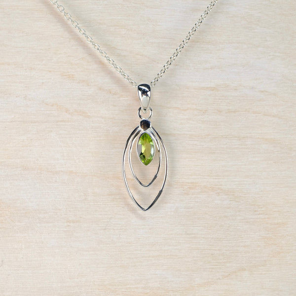 Silver pendant with a green gemstone on a light wood background