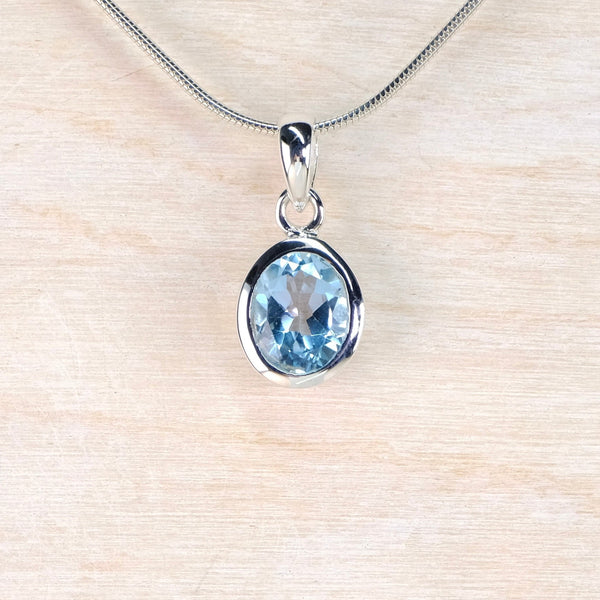 Silver pendant with a blue gemstone on a beige background
