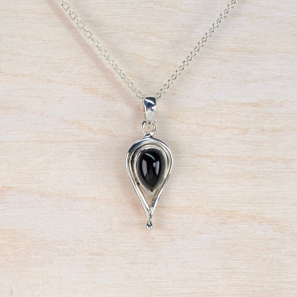 Silver pendant with black stone on a beige background