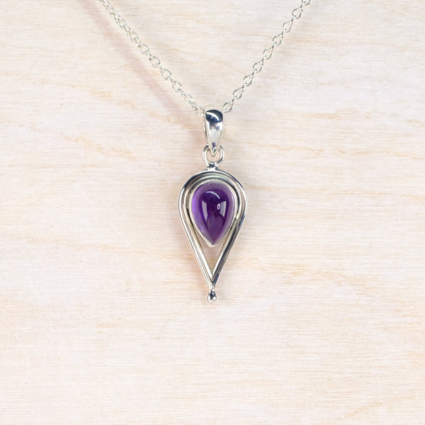 Silver necklace with a purple teardrop pendant on a light wood background