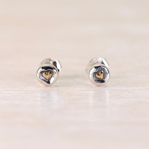 Heart-shaped silver earrings  with a gold hear at the centre on a light wooden surface 