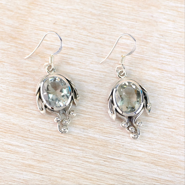 Silver earrings with green gemstones on a light wooden surface