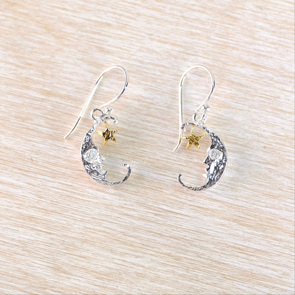 Silver earrings with star and moon designs on a light wood surface