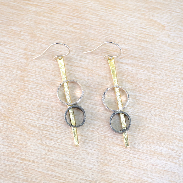Pair of earrings with circular and bar designs on a wooden surface