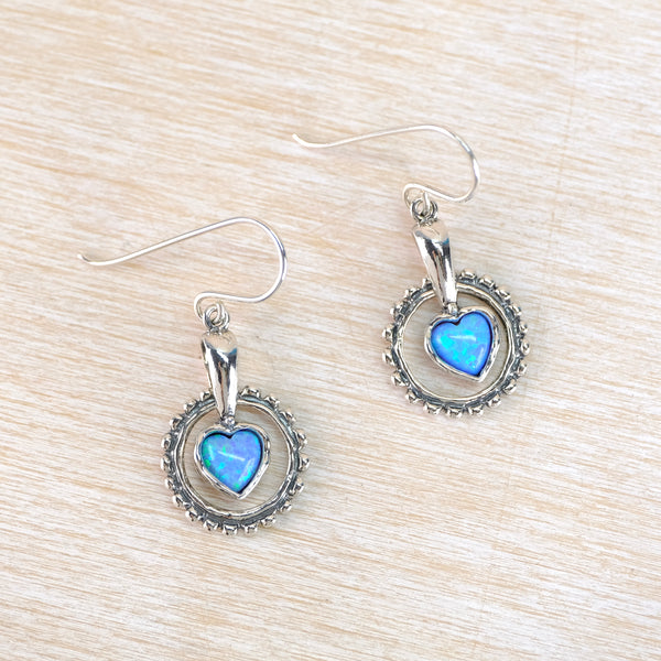 Silver earrings with blue heart-shaped stones on a beige surface