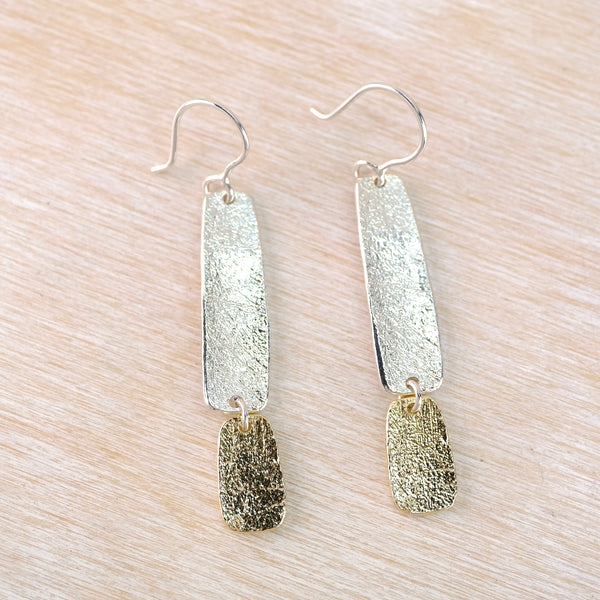 Pair of silver and gold  rectangular earrings on a light wood surface