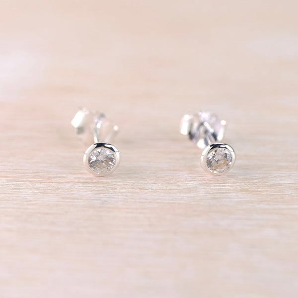 Pair of silver stud earrings with clear gemstones on a light beige background