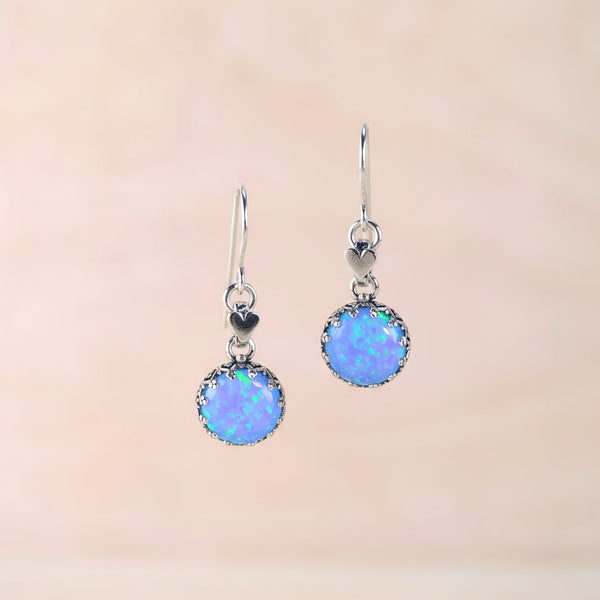 Pair of blue opal earrings on a stand against a beige background