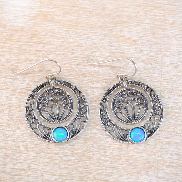Silver earrings with circular designs and blue gemstones on a wooden surface
