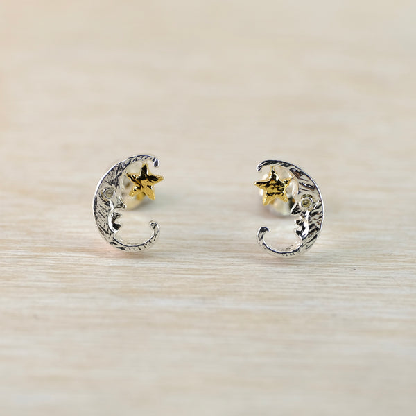 Pair of silver earrings with crescent moon and star designs on a light wooden surface