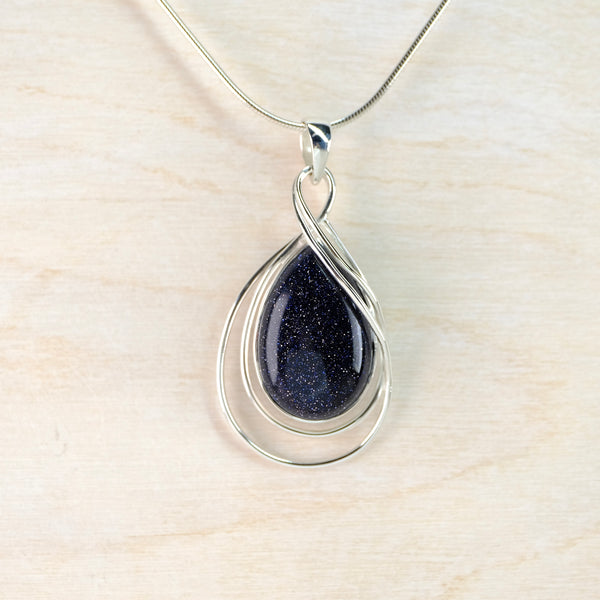 Silver pendant with a very dark blue teardrop-shaped stone on a light wood background