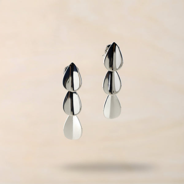 Pair of silver triple teardrop earrings against a beige background