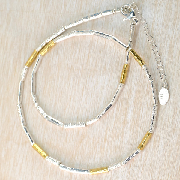 Silver and gold necklace on a light wood surface