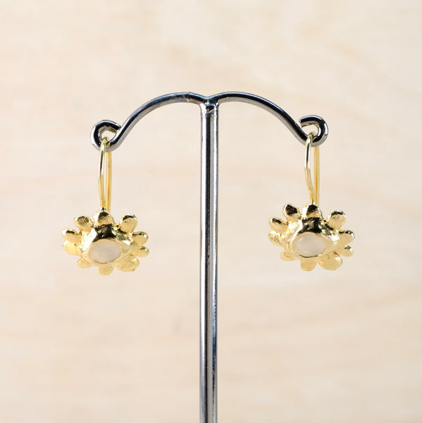 Gold earrings on a display stand against a beige background